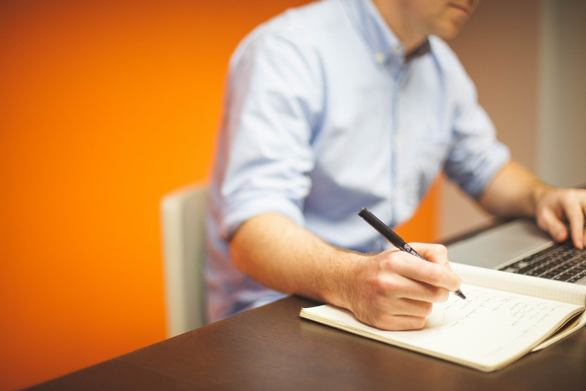 Man in shirt sat at desk with laptop and notepad: marketing