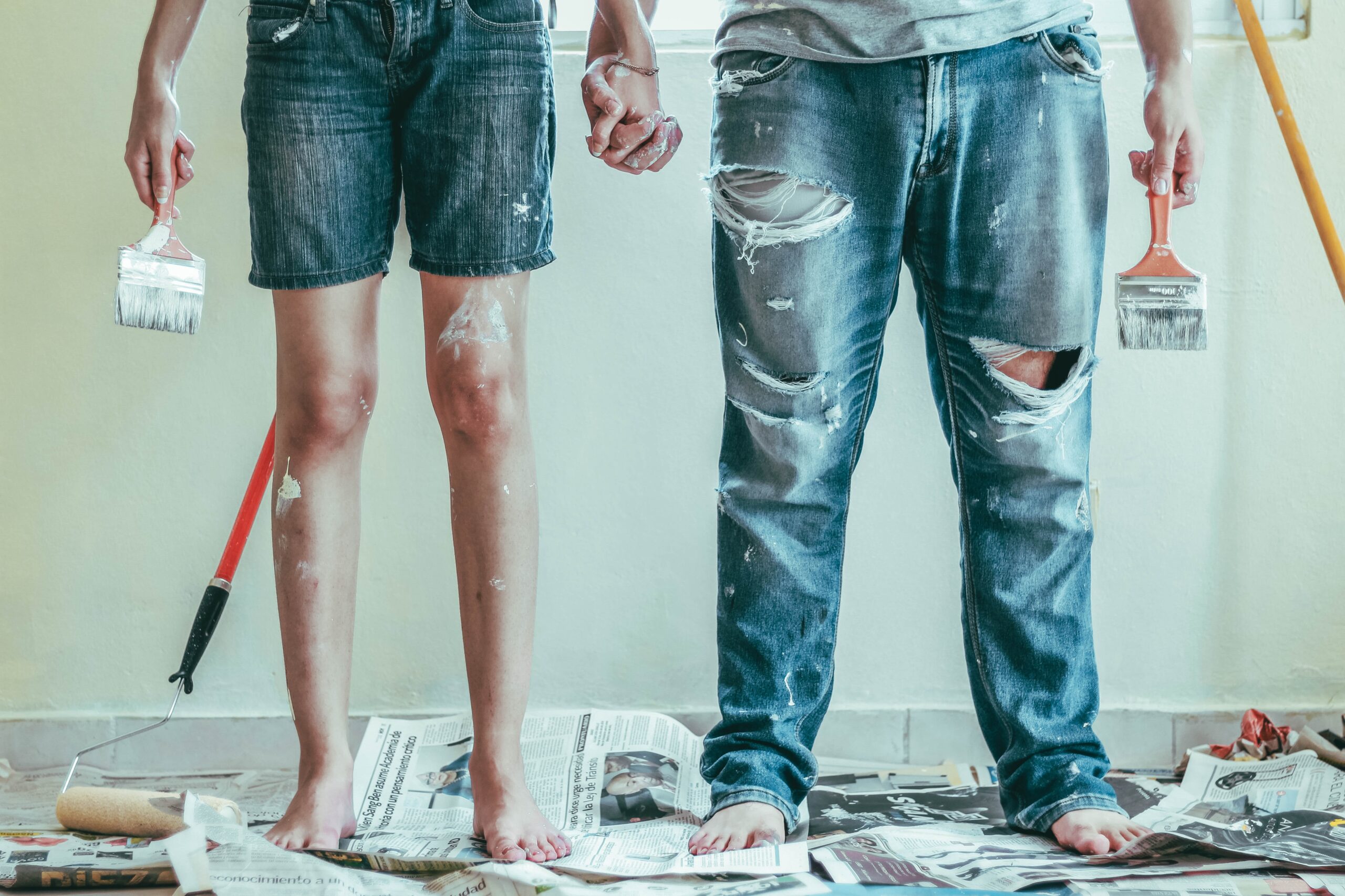 Man and woman holding hands with painting tools and paint over their clothes for DIY